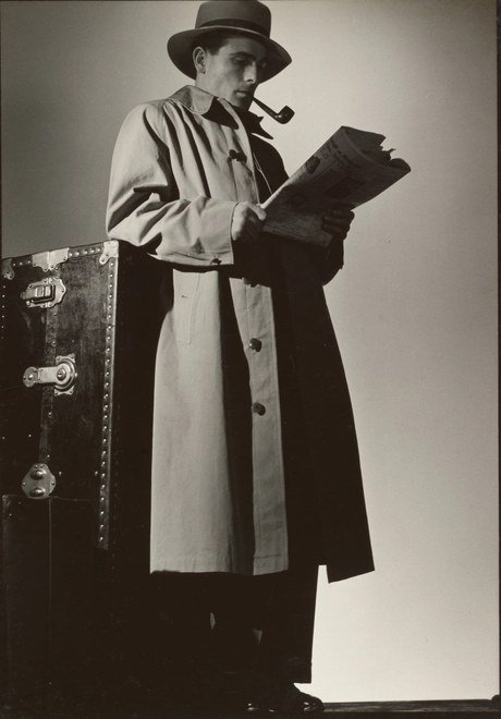 Investigator in a trench coat studying a newspaper